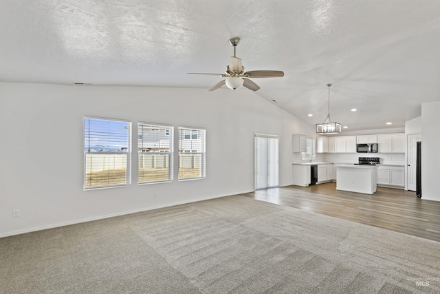 unfurnished living room featuring a ceiling fan, lofted ceiling, light carpet, and a textured ceiling