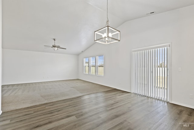 empty room with lofted ceiling, ceiling fan with notable chandelier, wood finished floors, and visible vents