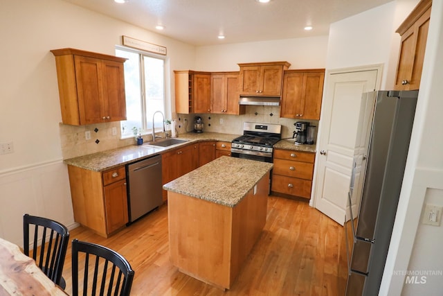 kitchen featuring a kitchen island, brown cabinets, a sink, under cabinet range hood, and stainless steel appliances