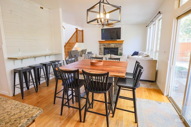 dining space with an inviting chandelier, light wood finished floors, a stone fireplace, stairs, and baseboards