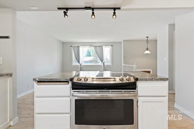 kitchen with track lighting, stainless steel range with electric cooktop, white cabinetry, light wood-style floors, and baseboards