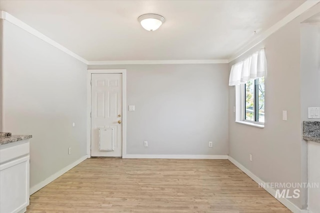 empty room featuring light wood finished floors, ornamental molding, and baseboards