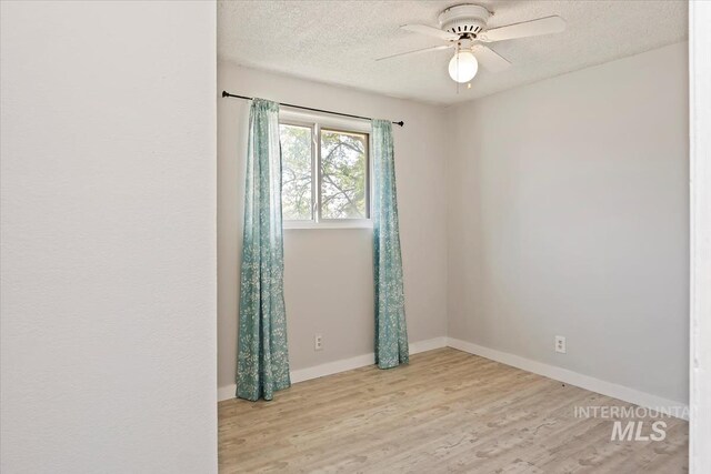 spare room featuring a textured ceiling, a ceiling fan, light wood-style flooring, and baseboards