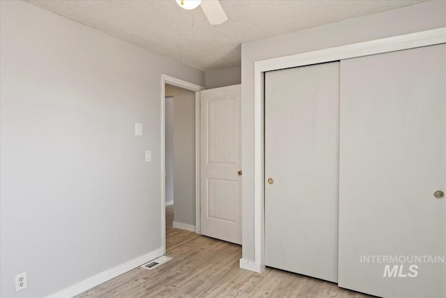 unfurnished bedroom with a closet, light wood finished floors, baseboards, visible vents, and a textured ceiling