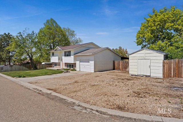 exterior space with an outdoor structure, concrete driveway, a storage unit, an attached garage, and fence