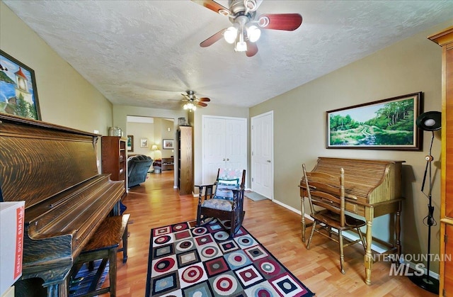 living area with light wood-style floors, baseboards, a ceiling fan, and a textured ceiling