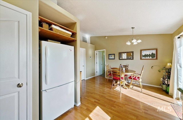 kitchen with light wood-style floors, a chandelier, freestanding refrigerator, baseboards, and visible vents