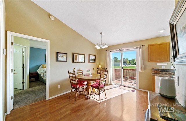 dining space with a notable chandelier, light wood finished floors, a textured ceiling, baseboards, and vaulted ceiling