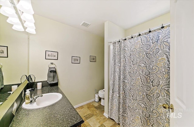 full bath with visible vents, vanity, toilet, baseboards, and stone finish flooring