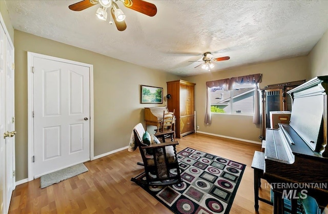 office area with light wood-type flooring, a ceiling fan, a textured ceiling, and baseboards
