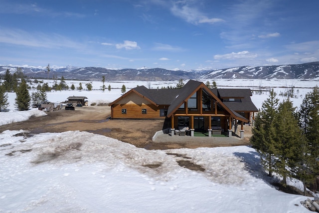 snow covered back of property with covered porch, faux log siding, and a mountain view