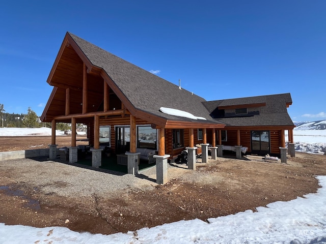 snow covered property with an outdoor hangout area, a patio area, and roof with shingles