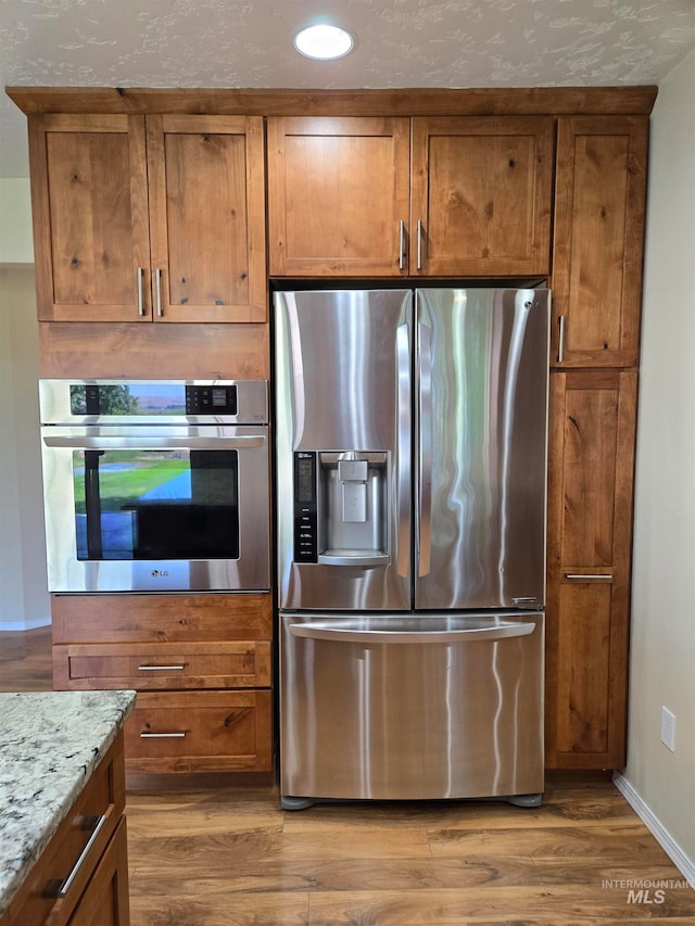 kitchen with hardwood / wood-style flooring, appliances with stainless steel finishes, and light stone counters