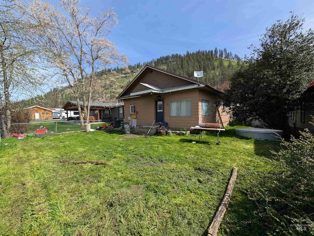 rear view of house with a mountain view, fence, and a yard