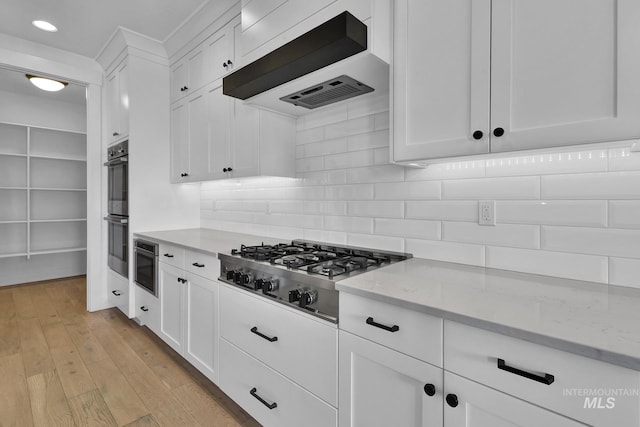 kitchen featuring stainless steel gas stovetop, white cabinets, custom range hood, backsplash, and light stone countertops