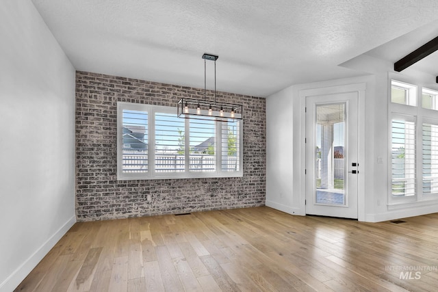 unfurnished dining area featuring brick wall, a textured ceiling, hardwood / wood-style floors, baseboards, and a chandelier