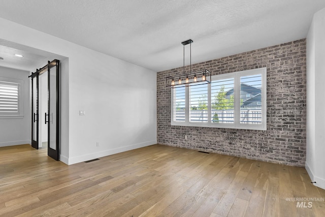 unfurnished dining area featuring light wood-style floors, brick wall, baseboards, a textured ceiling, and a barn door