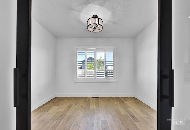 unfurnished room featuring baseboards, light wood-style floors, a textured ceiling, and a chandelier