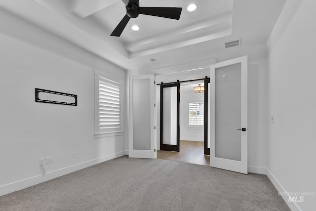 unfurnished bedroom with carpet, a raised ceiling, a barn door, recessed lighting, and baseboards