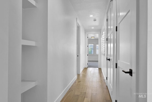 corridor with a textured ceiling, baseboards, light wood-style floors, and recessed lighting
