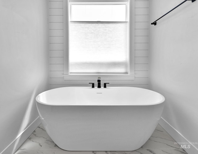 bathroom with marble finish flooring, baseboards, and a soaking tub