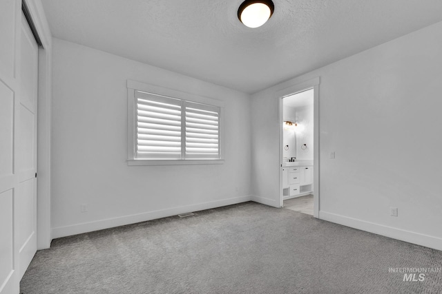 unfurnished bedroom featuring baseboards, light carpet, connected bathroom, a textured ceiling, and a sink