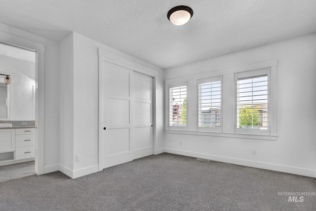 unfurnished bedroom with baseboards, a closet, a textured ceiling, and carpet floors