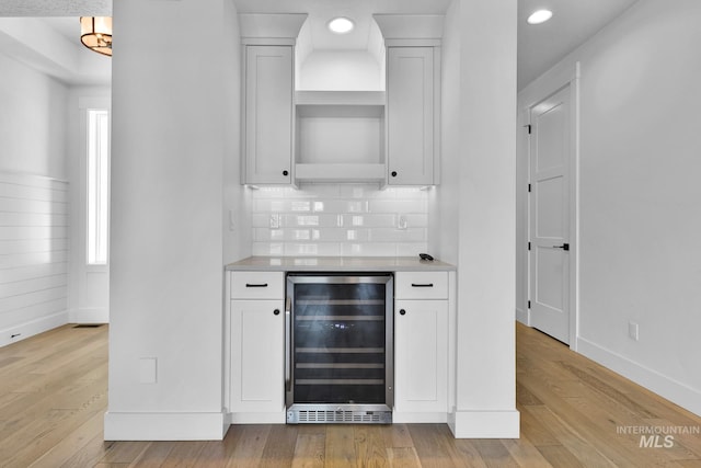indoor dry bar with beverage cooler, light wood-style floors, baseboards, decorative backsplash, and recessed lighting