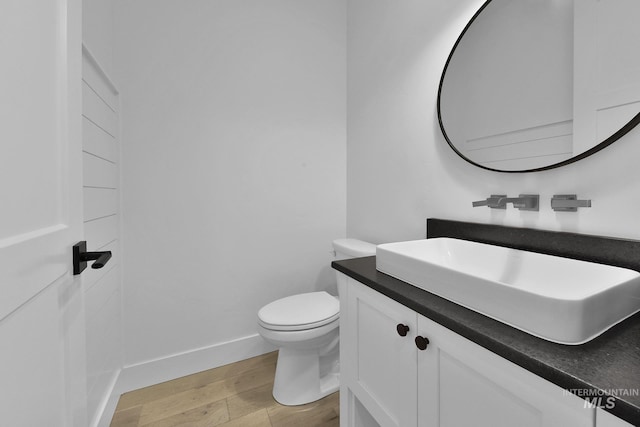 half bath with wood finished floors, toilet, vanity, and baseboards