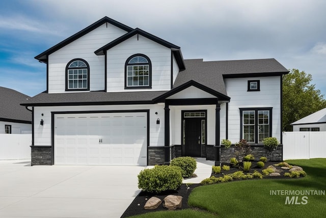 view of front of home featuring an attached garage, fence, stone siding, driveway, and roof with shingles