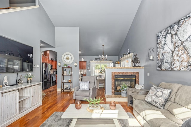 living area featuring arched walkways, dark wood-style flooring, an inviting chandelier, a high end fireplace, and high vaulted ceiling