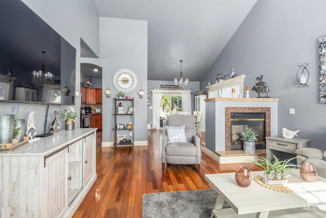 living area with a notable chandelier, a high end fireplace, wood finished floors, high vaulted ceiling, and baseboards