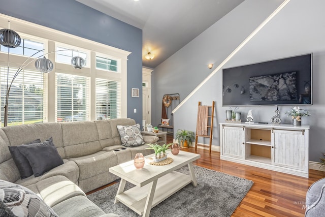 living room with light wood-type flooring, vaulted ceiling, plenty of natural light, and baseboards