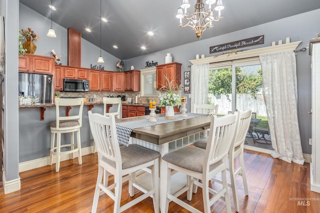 dining area featuring high vaulted ceiling, a notable chandelier, baseboards, and hardwood / wood-style flooring