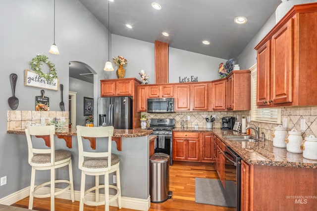 kitchen with arched walkways, stainless steel appliances, light wood-type flooring, a kitchen bar, and a sink