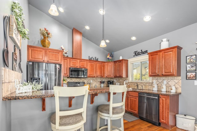 kitchen featuring lofted ceiling, wood finished floors, hanging light fixtures, appliances with stainless steel finishes, and a kitchen bar