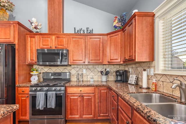 kitchen featuring tasteful backsplash, dark stone counters, lofted ceiling, stainless steel appliances, and a sink