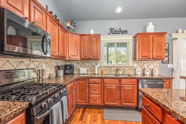 kitchen featuring light wood-type flooring, appliances with stainless steel finishes, dark stone counters, and a sink