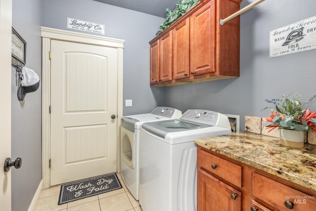 clothes washing area with cabinet space, light tile patterned floors, and washer and clothes dryer