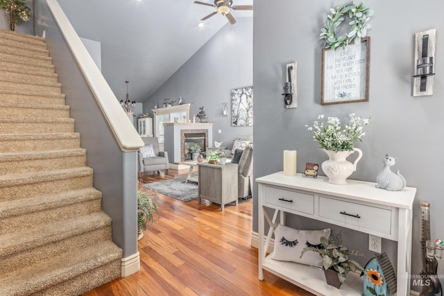 interior space featuring stairway, a ceiling fan, a glass covered fireplace, high vaulted ceiling, and light wood-type flooring