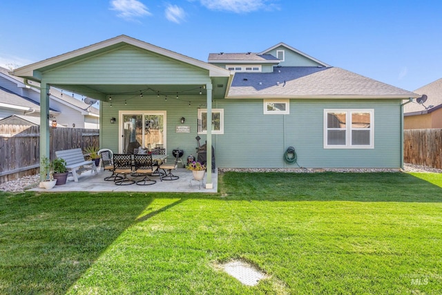 back of house with a shingled roof, a patio area, a lawn, and a fenced backyard