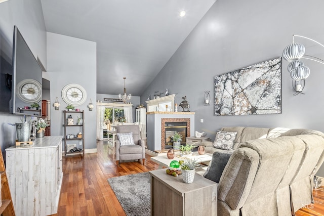 living area with a chandelier, a glass covered fireplace, wood finished floors, high vaulted ceiling, and baseboards