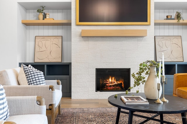 living area featuring a tiled fireplace, built in shelves, and wood finished floors