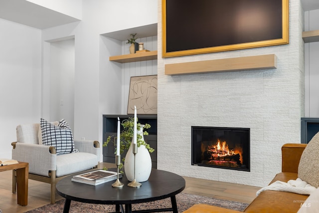 sitting room with built in features, a tiled fireplace, wood finished floors, and a towering ceiling