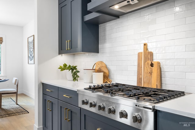 kitchen with stainless steel gas cooktop, baseboards, light countertops, wall chimney exhaust hood, and tasteful backsplash