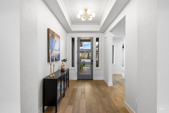 foyer entrance with hardwood / wood-style flooring, a notable chandelier, baseboards, and a raised ceiling