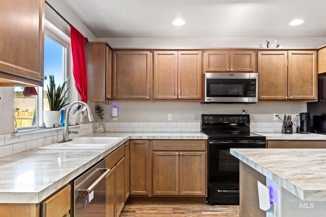 kitchen with appliances with stainless steel finishes, a sink, light countertops, light wood-type flooring, and recessed lighting