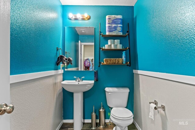 half bathroom with toilet, wood finished floors, and a sink