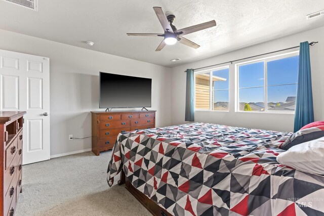 bedroom with light colored carpet, ceiling fan, baseboards, and a textured ceiling