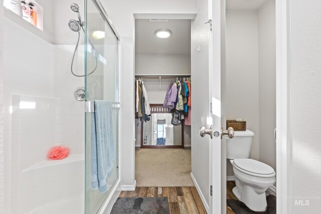 bathroom featuring wood finished floors, a stall shower, toilet, and a spacious closet